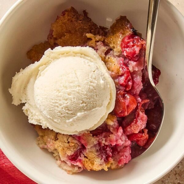 White bowl filled with serving of cherry cobbler with spoon.
