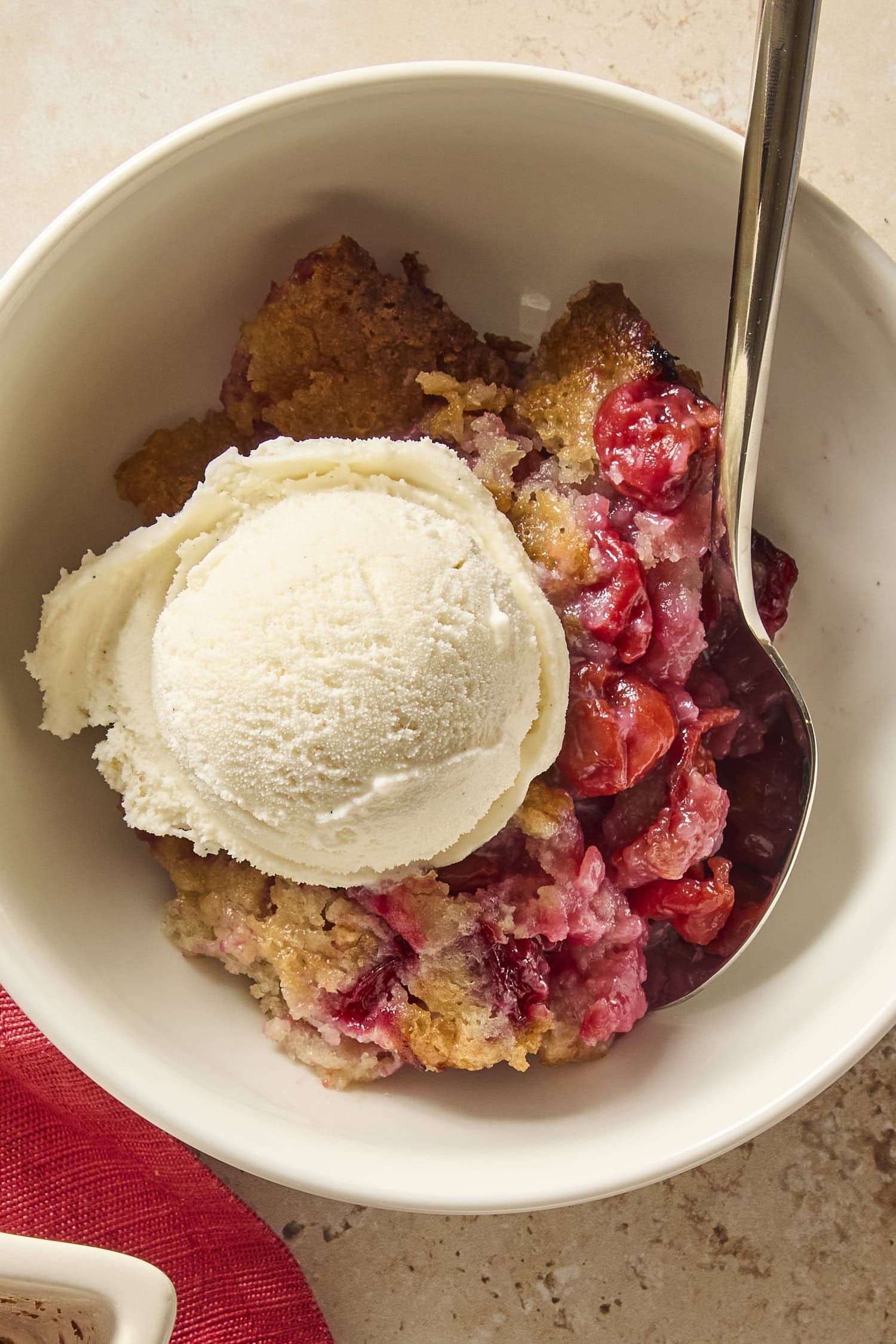 Bowl with scoop of vanilla ice cream on top of cherry cobbler.