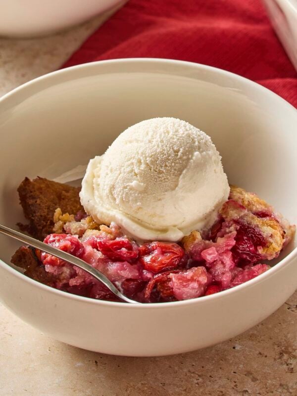 White bowl filled with cherry cobbler with scoop of vanilla ice cream on top.
