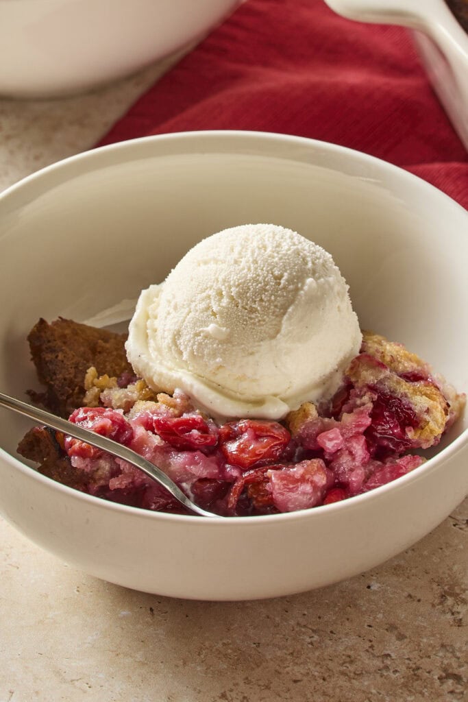 White bowl filled with cherry cobbler with scoop of vanilla ice cream on top.