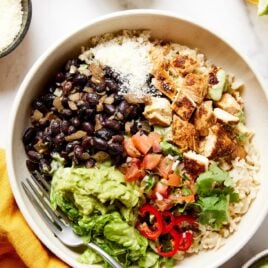 White bowl filled with rice, chicken, salsa, lettuce, and more.