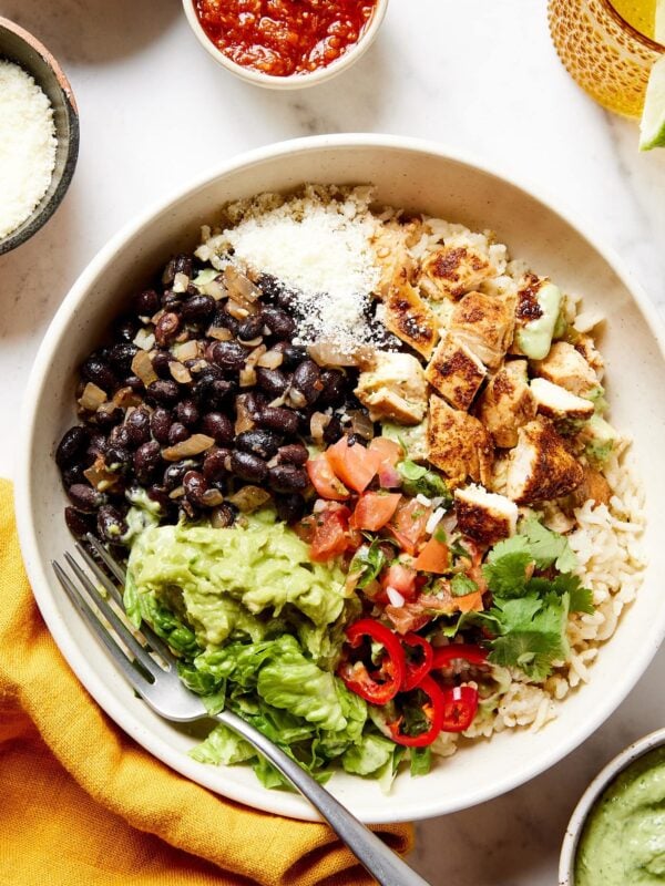 White bowl filled with rice, chicken, salsa, lettuce, and more.