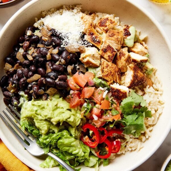 White bowl filled with chicken meat cooked with rice and topped with beans.