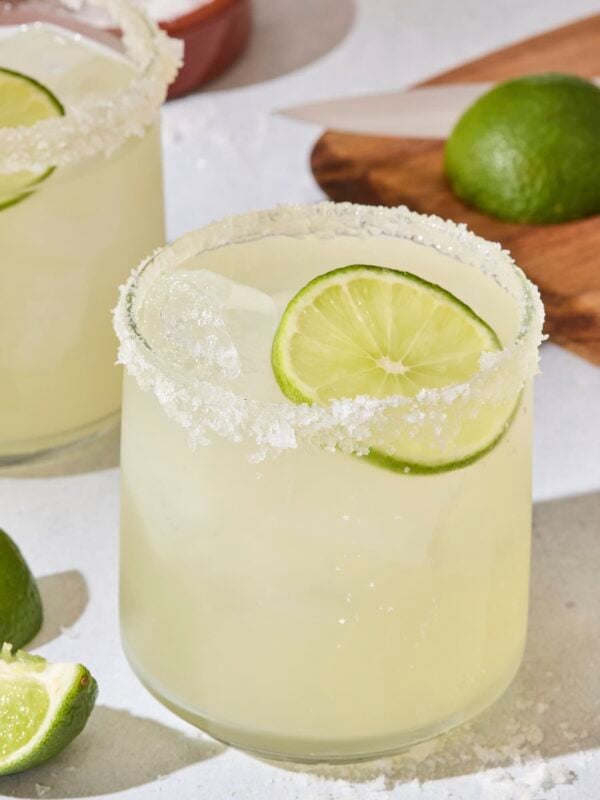 Cocktail glass filled with light green colored margarita with salt rim and lime slice.