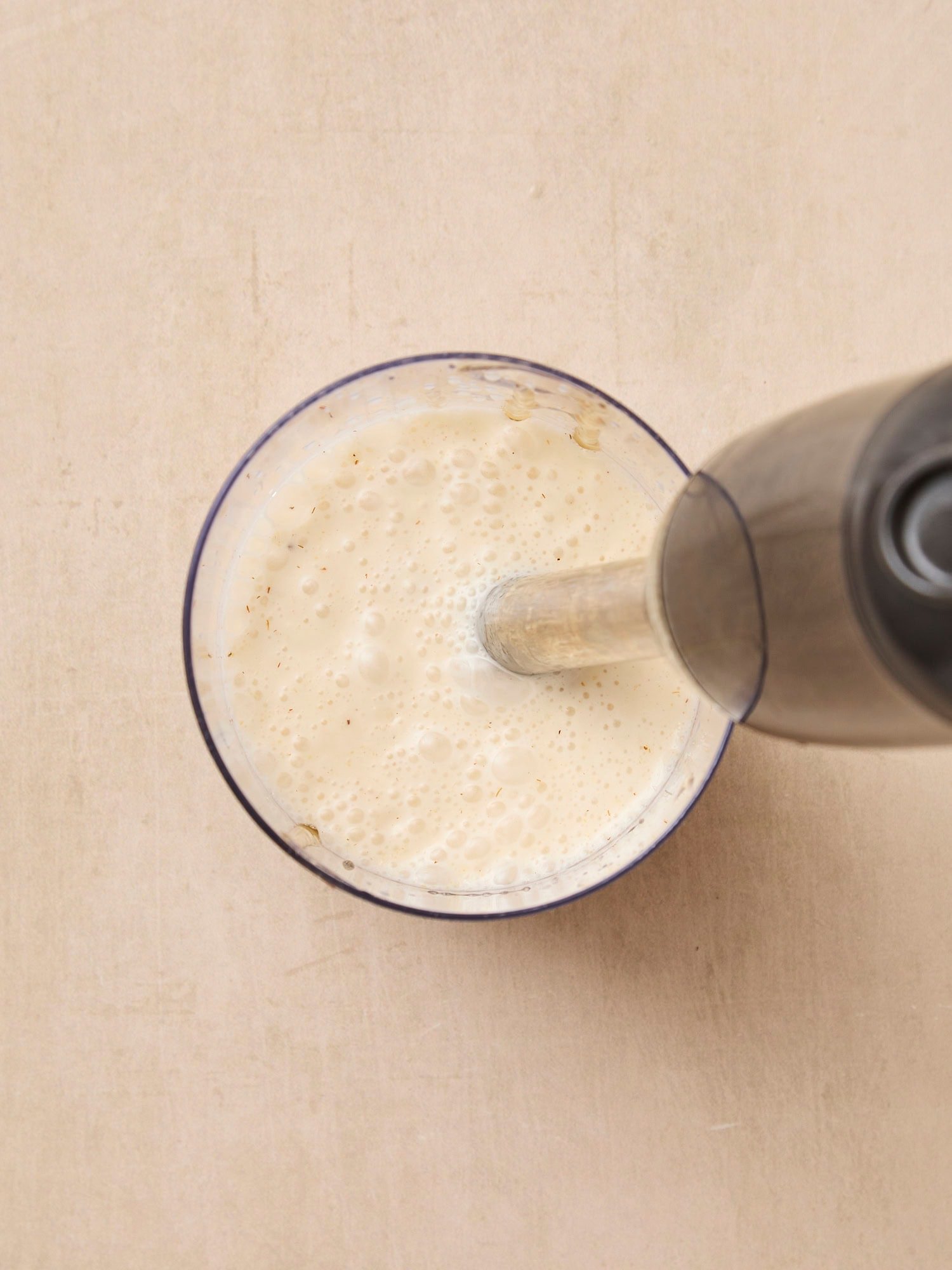 Handheld blender mixing up coleslaw dressing with a creamy texture.