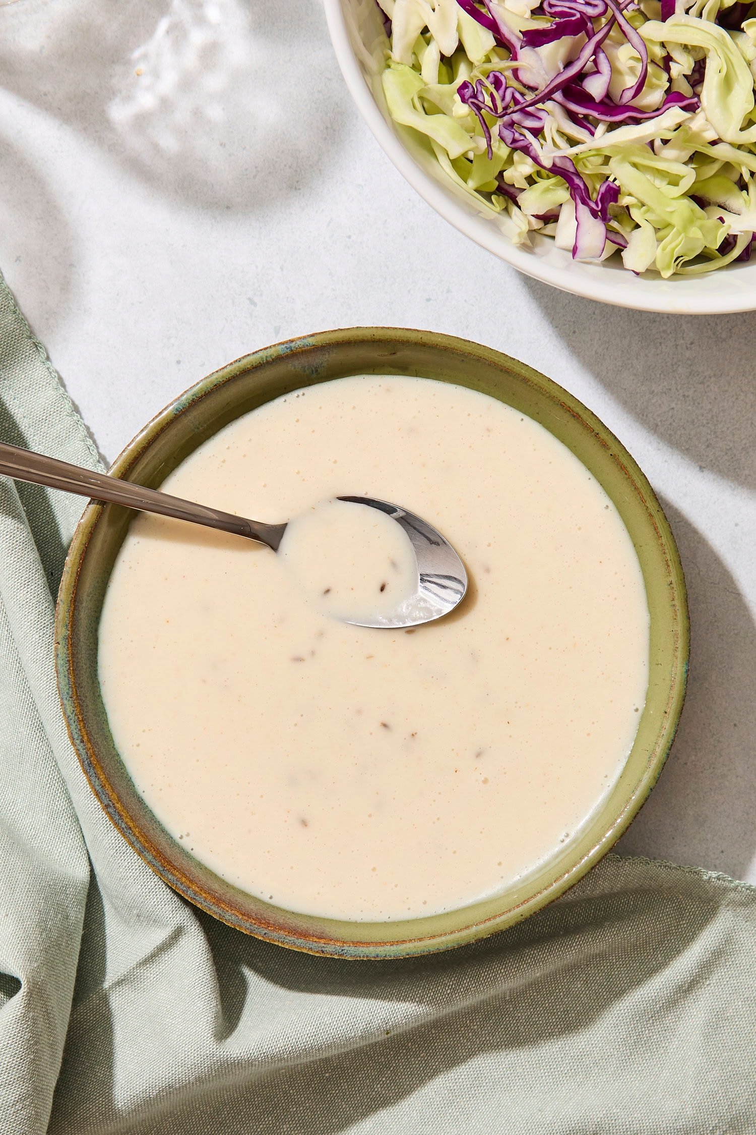 Green bowl filled with coleslaw dressing with spoon scooping out a serving.