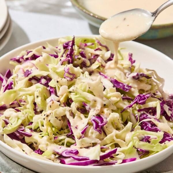 Spoon drizzling dressing over the top of shredded cabbage in a bowl.