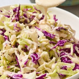 Cabbage with a creamy coleslaw dressing being poured over the top.