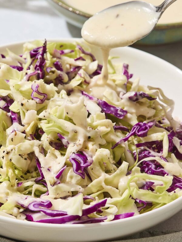 Cabbage with a creamy coleslaw dressing being poured over the top.