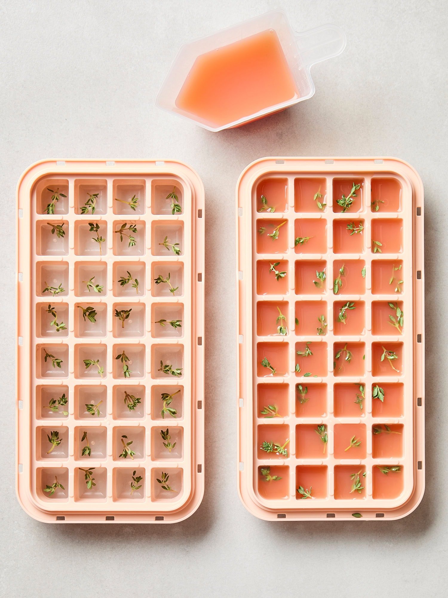 Two ice cube trays filled with fresh thyme and grapefruit juice.