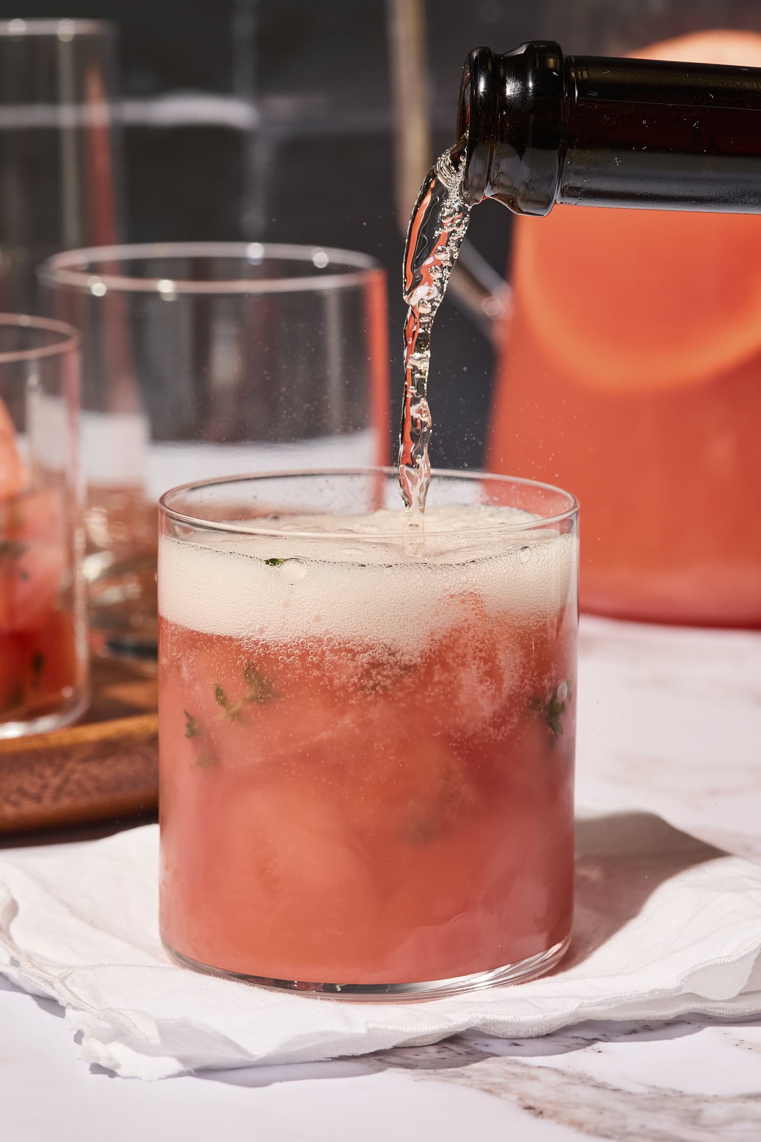 Bottle of sparkling wine pouring on top of a pink punch in a glass.