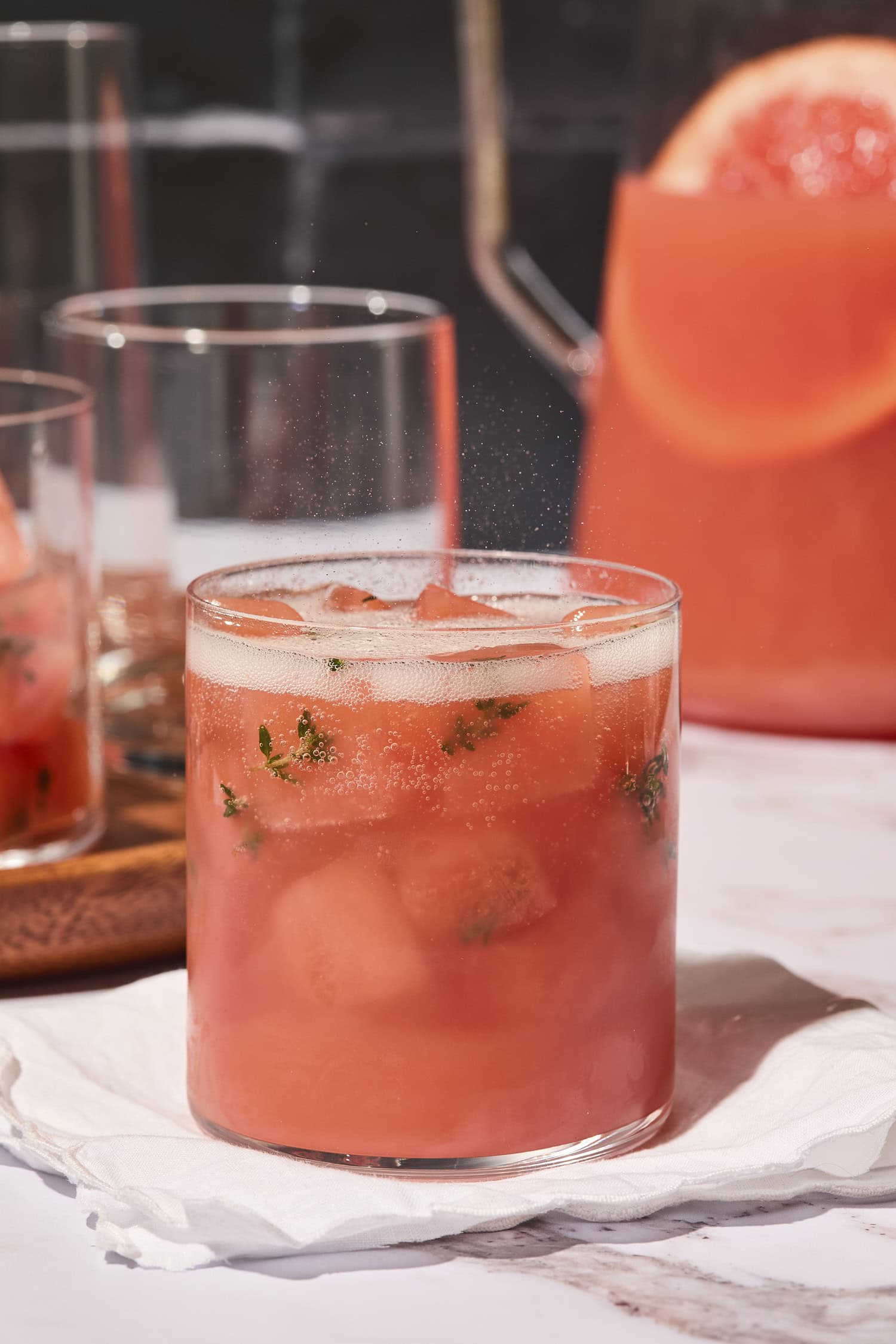 Glass of sparkling pink punch with ice cubes with a bit of thyme frozen in them.