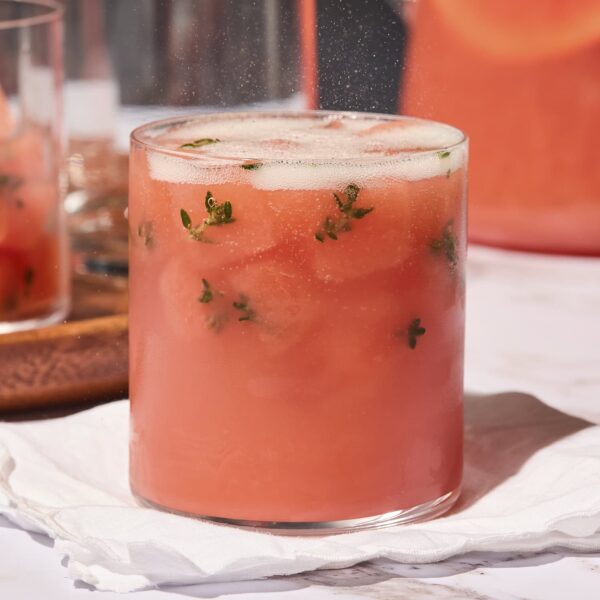 Glass filled with a grapefruit gin punch with thyme leaves and topped with sparkling wine.