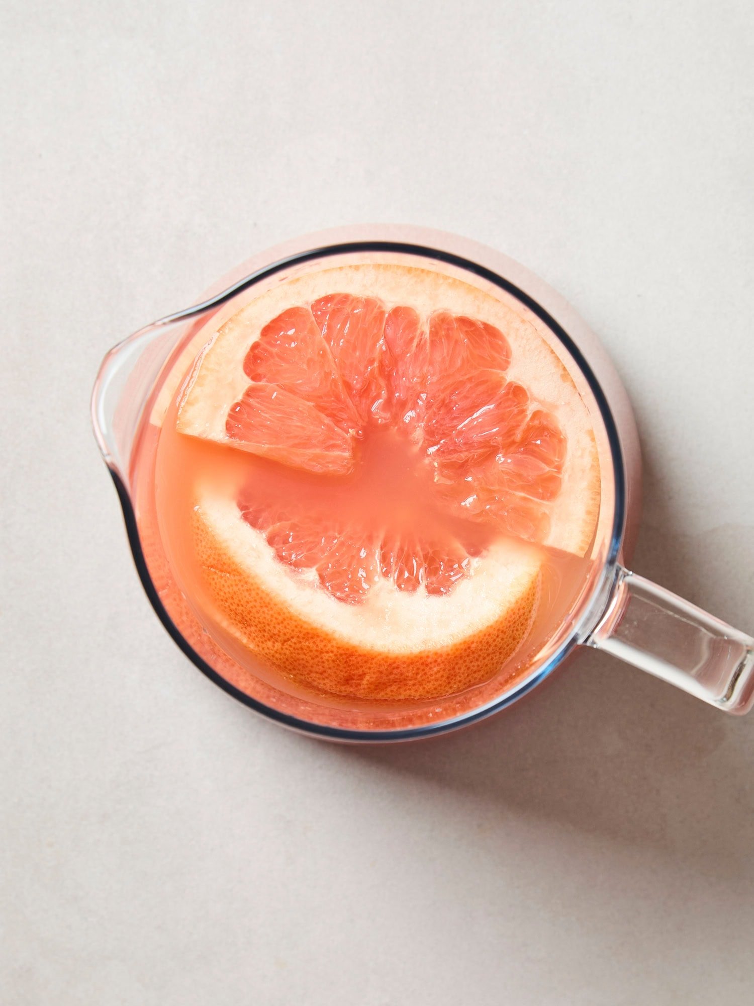 A glass pitcher filled with grapefruit juice with grapefruit slices on top.