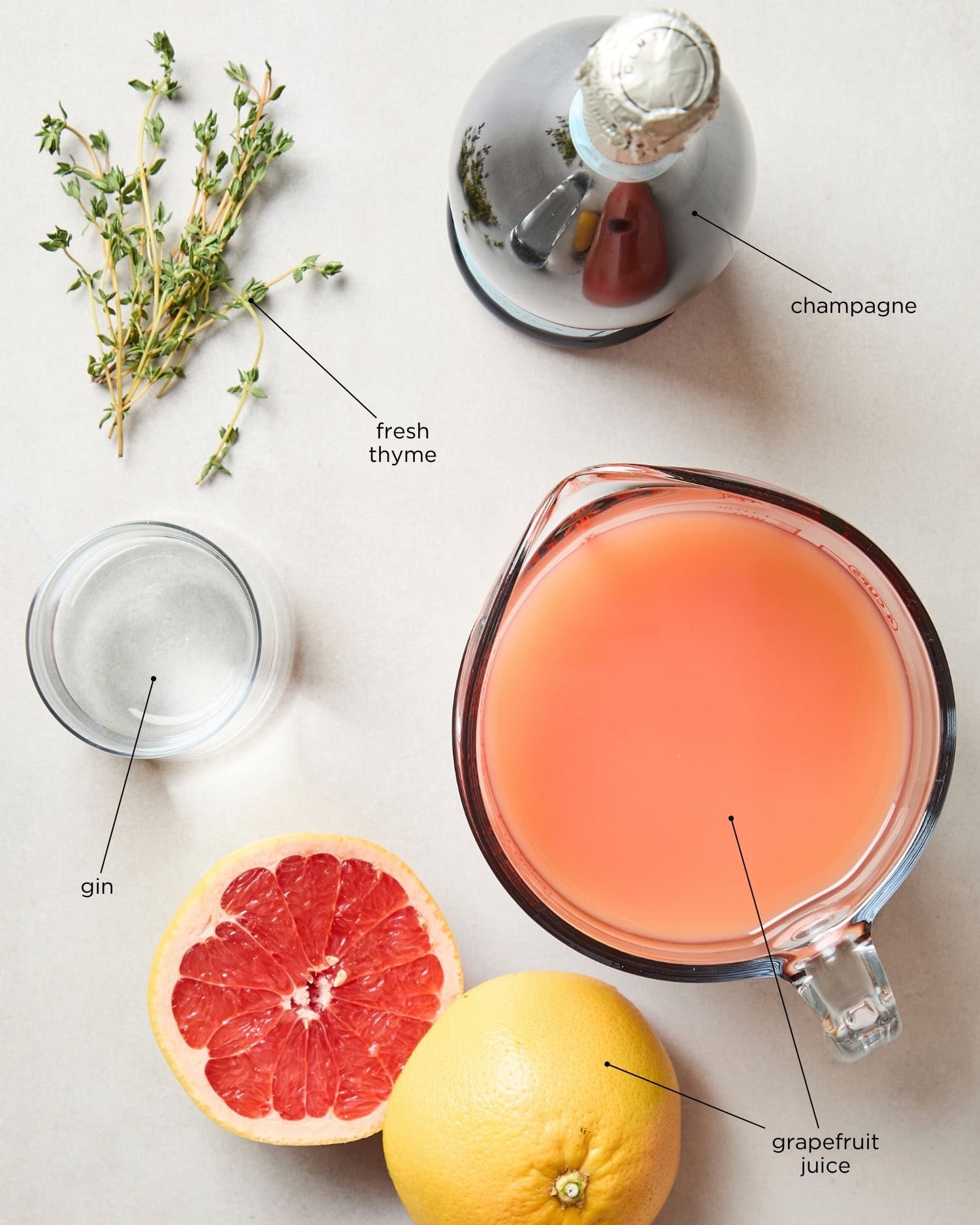 Surface with ingredients needed for a grapefruit gin punch including juice, champagne, gin, and thyme.