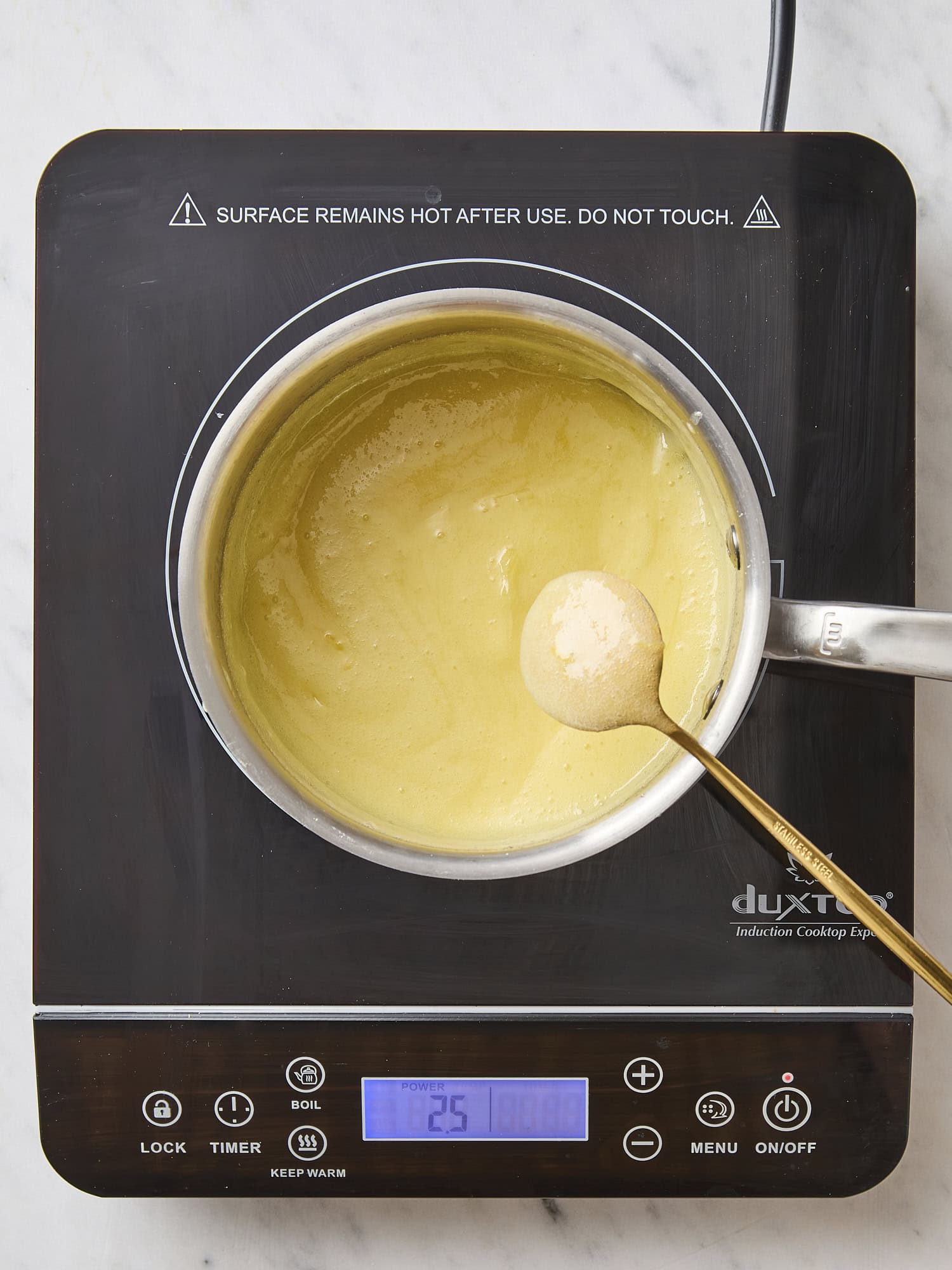 Cooktop with creamy lemon curd with spoon showing consistency.