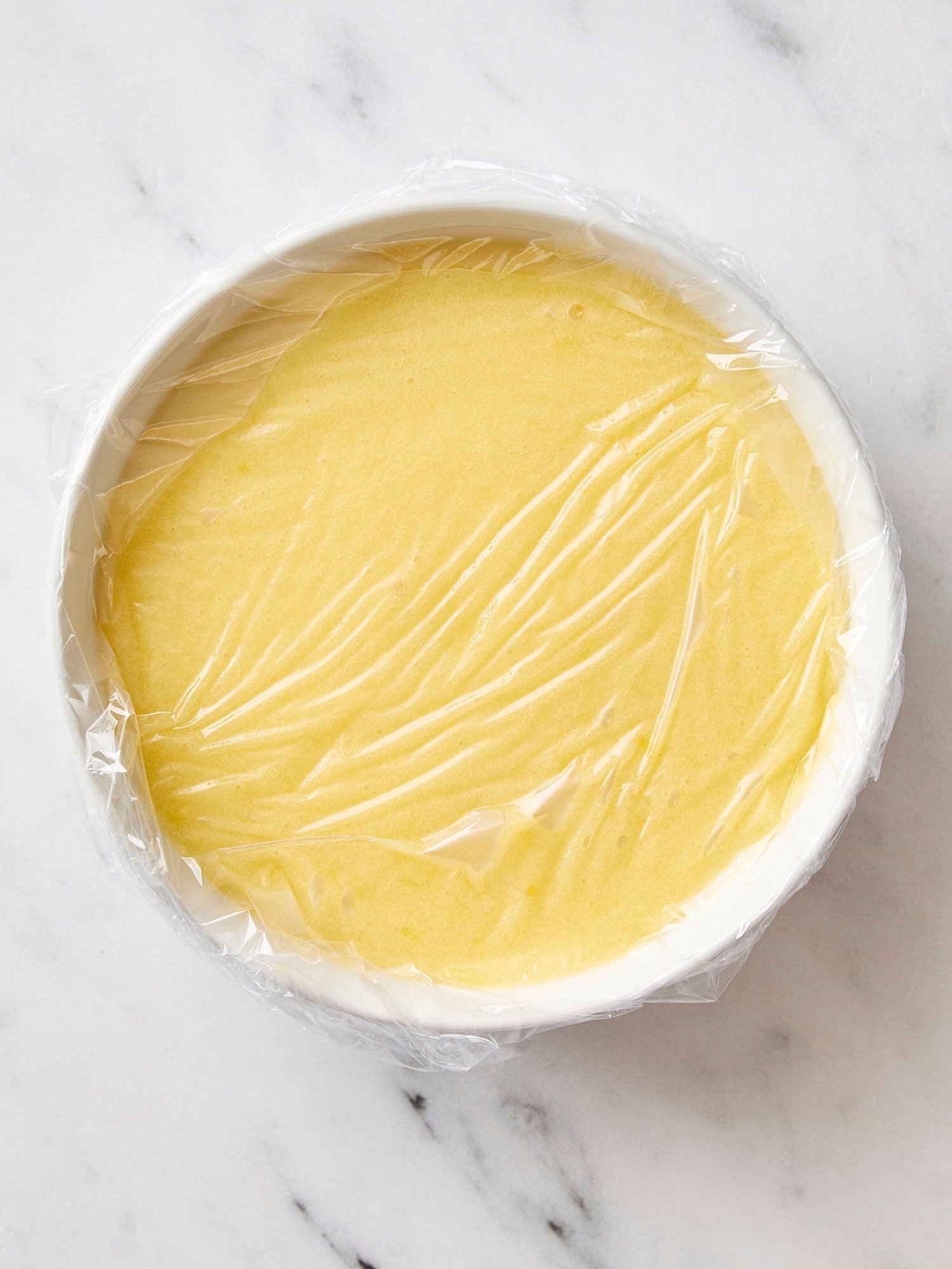 White bowl with plastic wrap on the surface of lemon curd.
