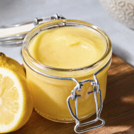 Container with light yellow lemon curd sitting on a cutting board.
