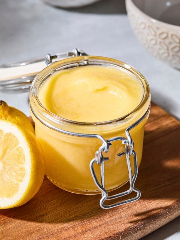 Container with light yellow lemon curd sitting on a cutting board.