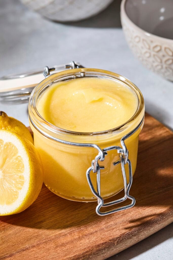 Container with light yellow lemon curd sitting on a cutting board.