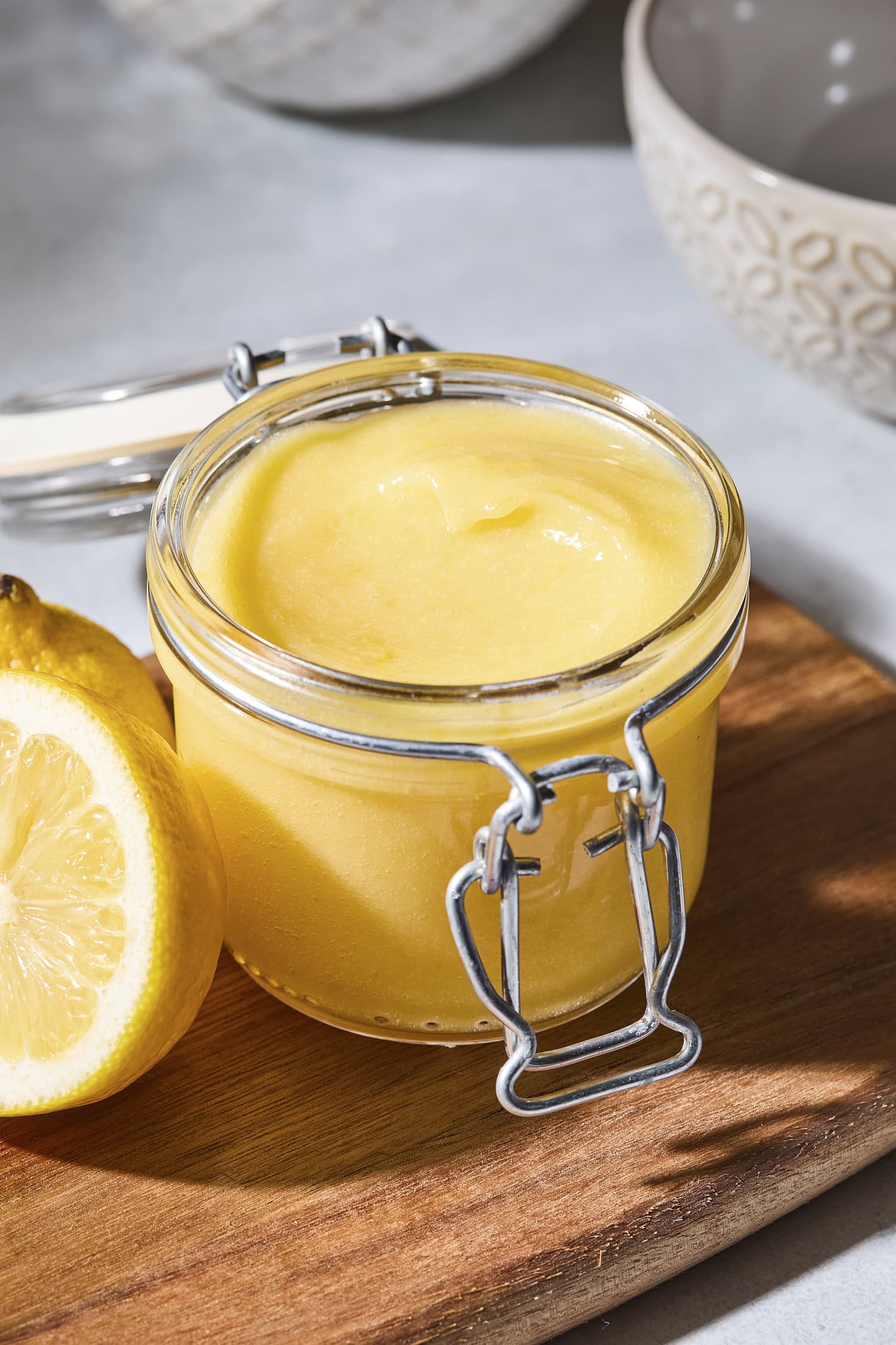 Container with light yellow lemon curd sitting on a cutting board.