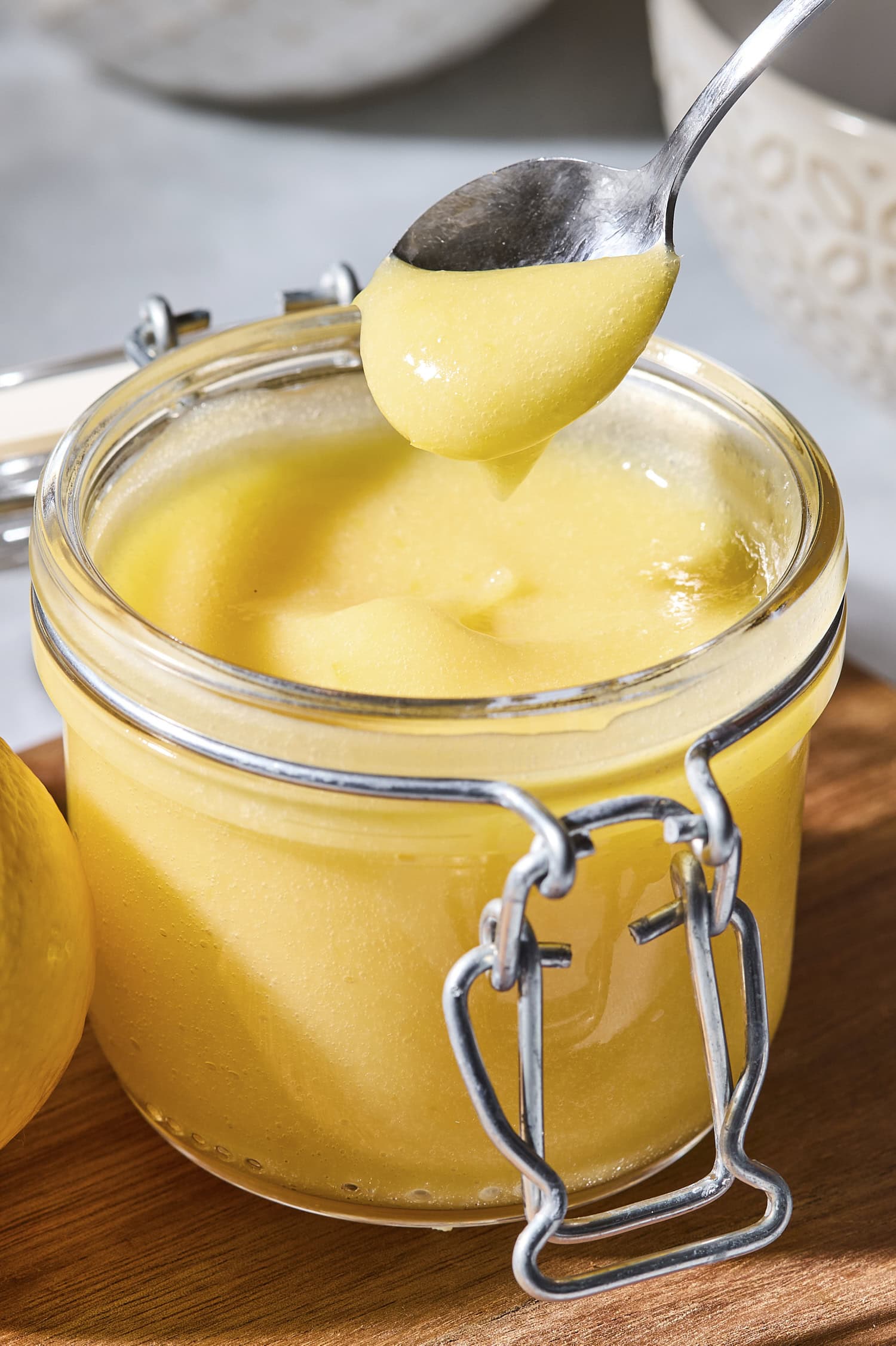 Glass container filled with lemon curd with spoon dolloping some.