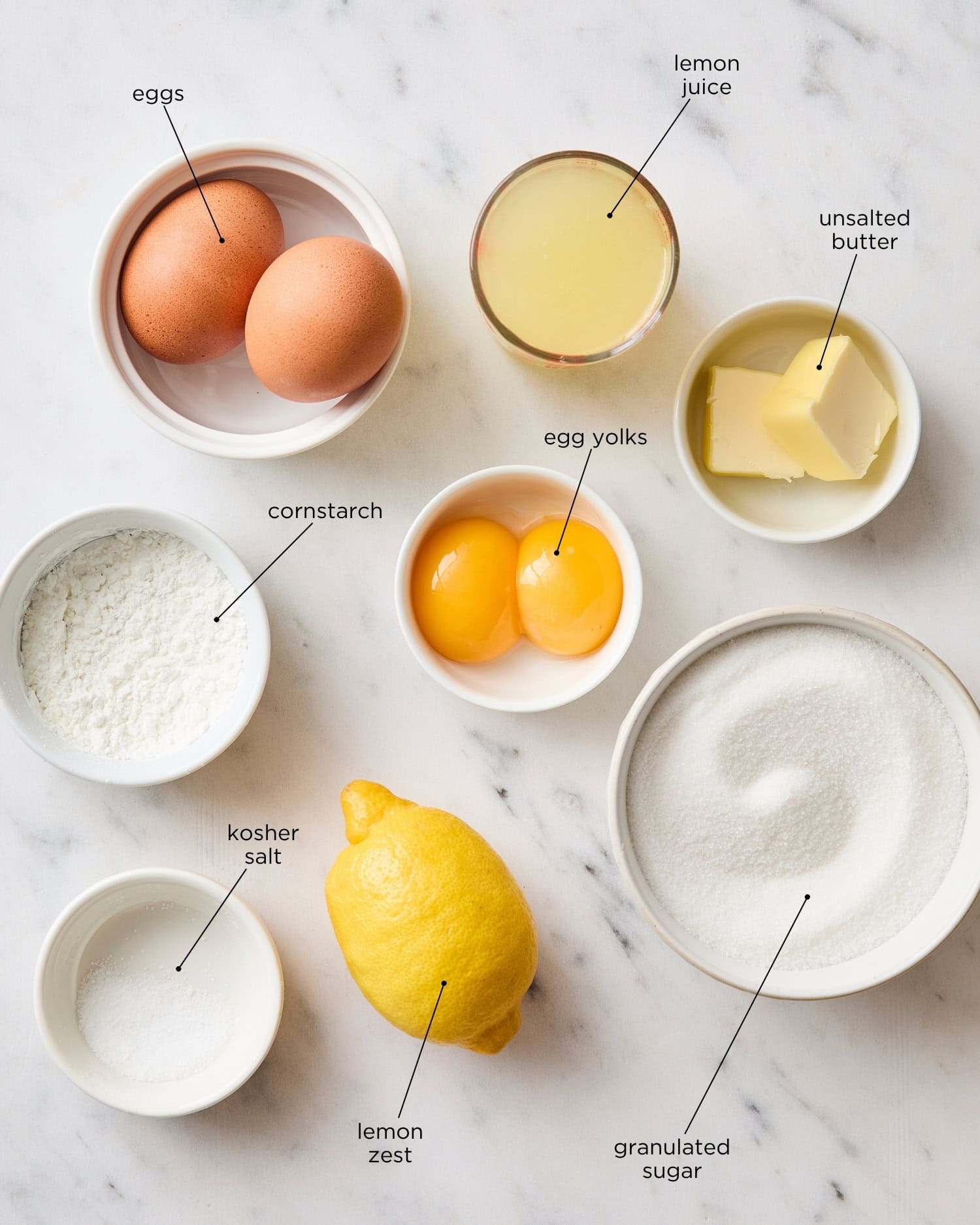 White marble surface filled with ingredients to make lemon curd including eggs, egg yolks, sugar, and more.