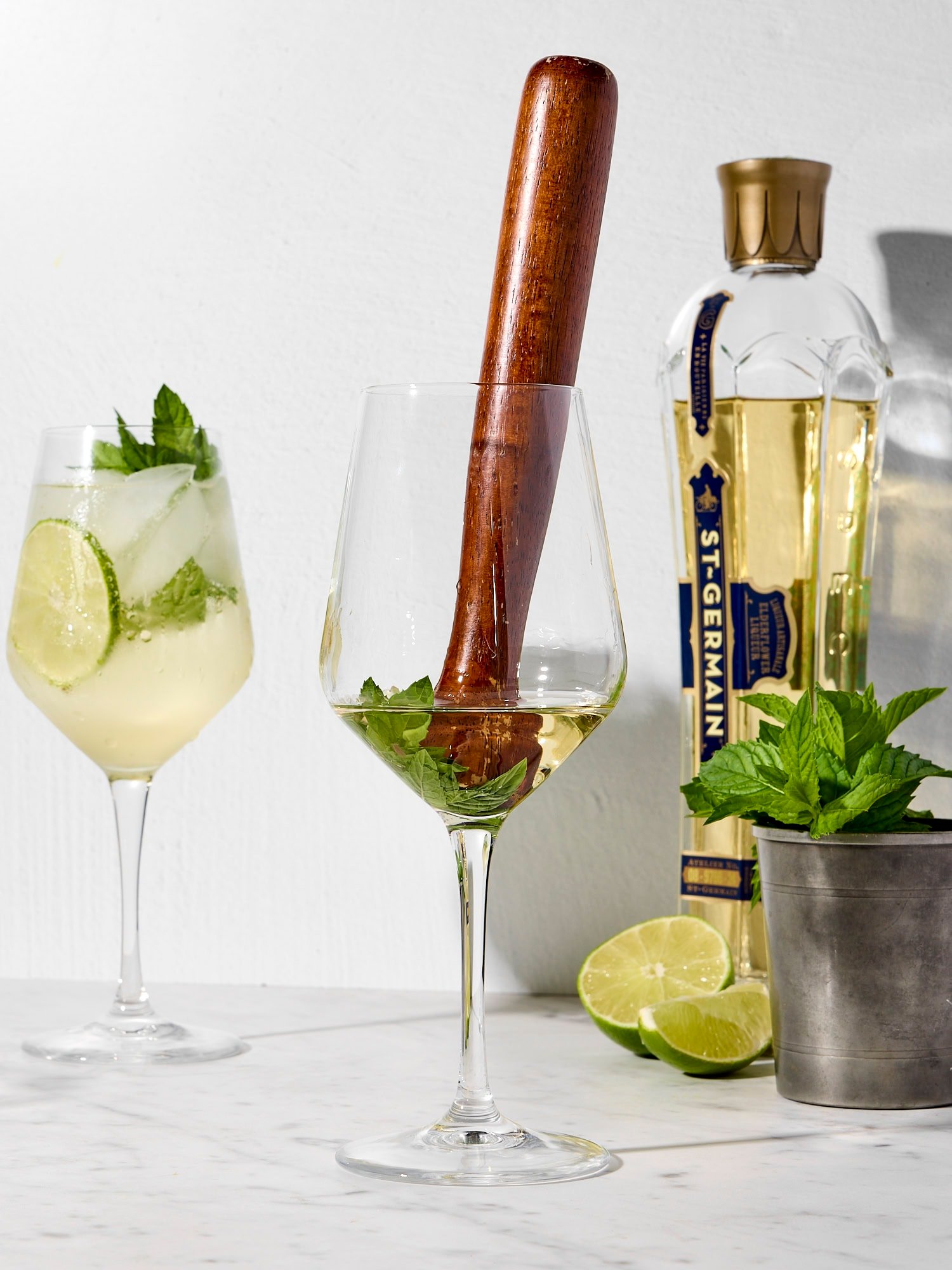 Wooden muddle mixing together mint with elderflower liqueur.