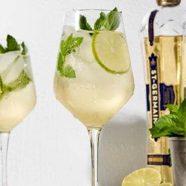 Wine glass filled with Hugo Spritz with mint sprig and lime wheel.