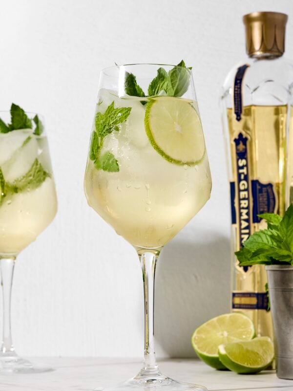Wine glass filled with Hugo Spritz with mint sprig and lime wheel.