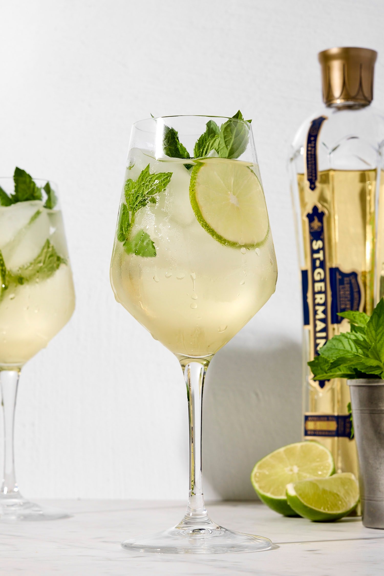 Wine glass filled with Hugo Spritz with mint sprig and lime wheel.