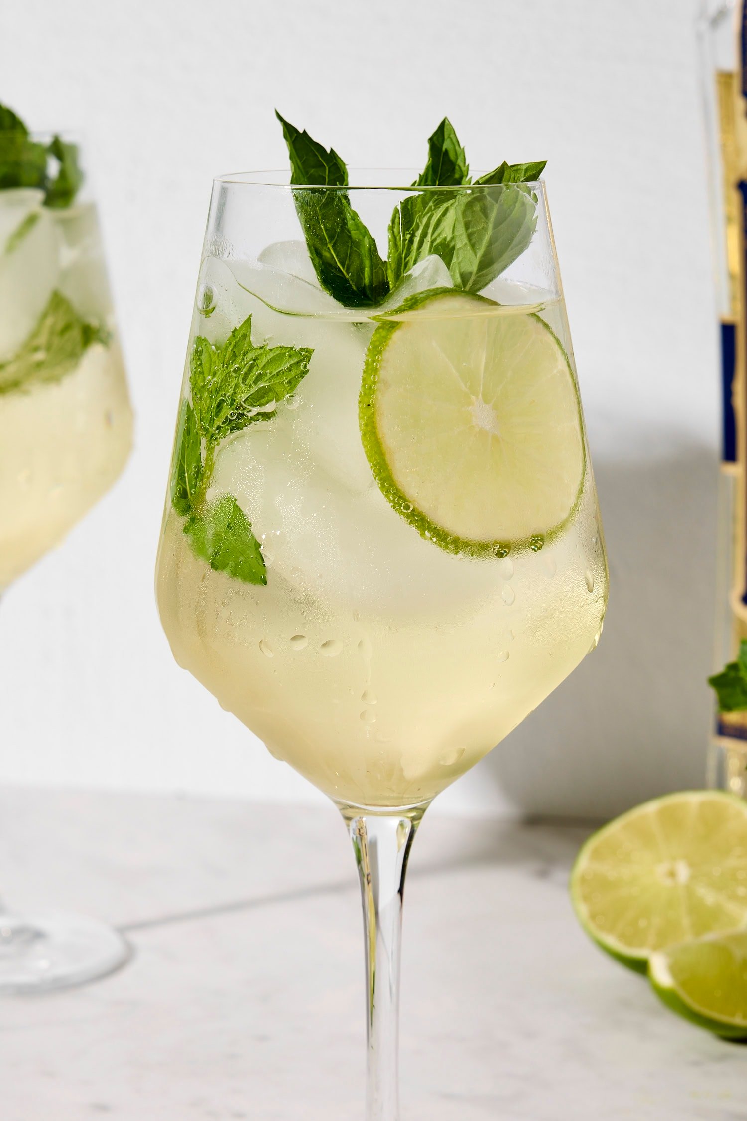 Wine glass with lime wheel and mint sprig and Hugo spritz inside.