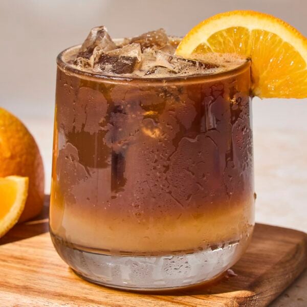Glass filled with orange espresso tonic with orange slice on rim.