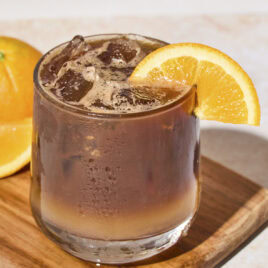 Glass filled with espresso and tonic with orange slice on rim.