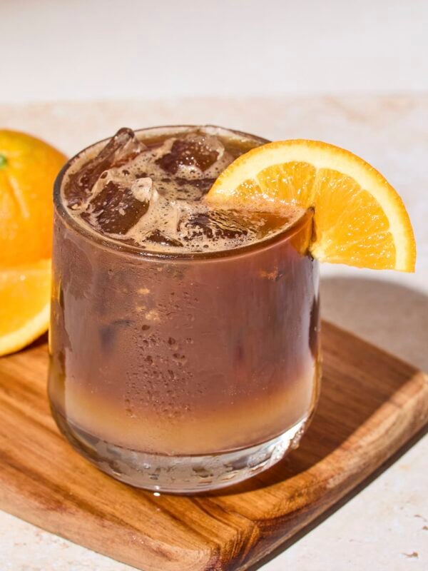 Glass filled with espresso and tonic with orange slice on rim.