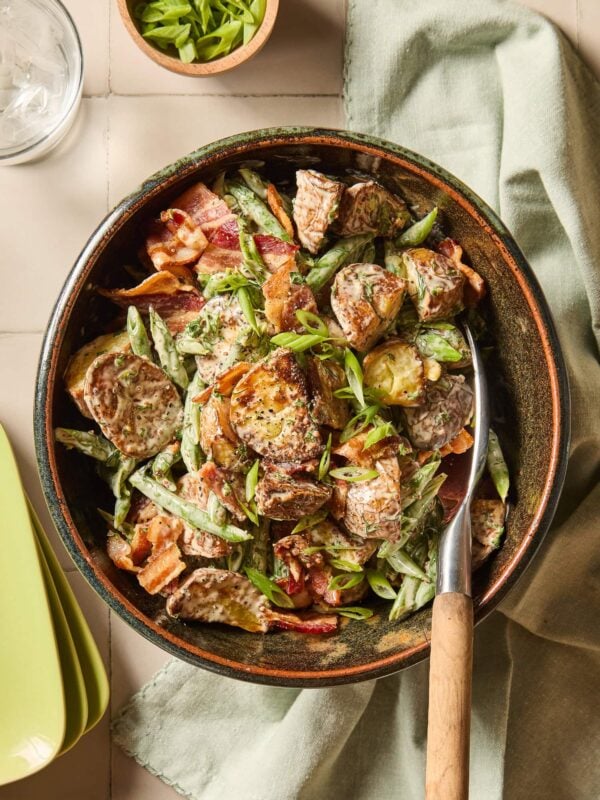 A bowl full of green bean and potato salad in a bowl on a tiled table.