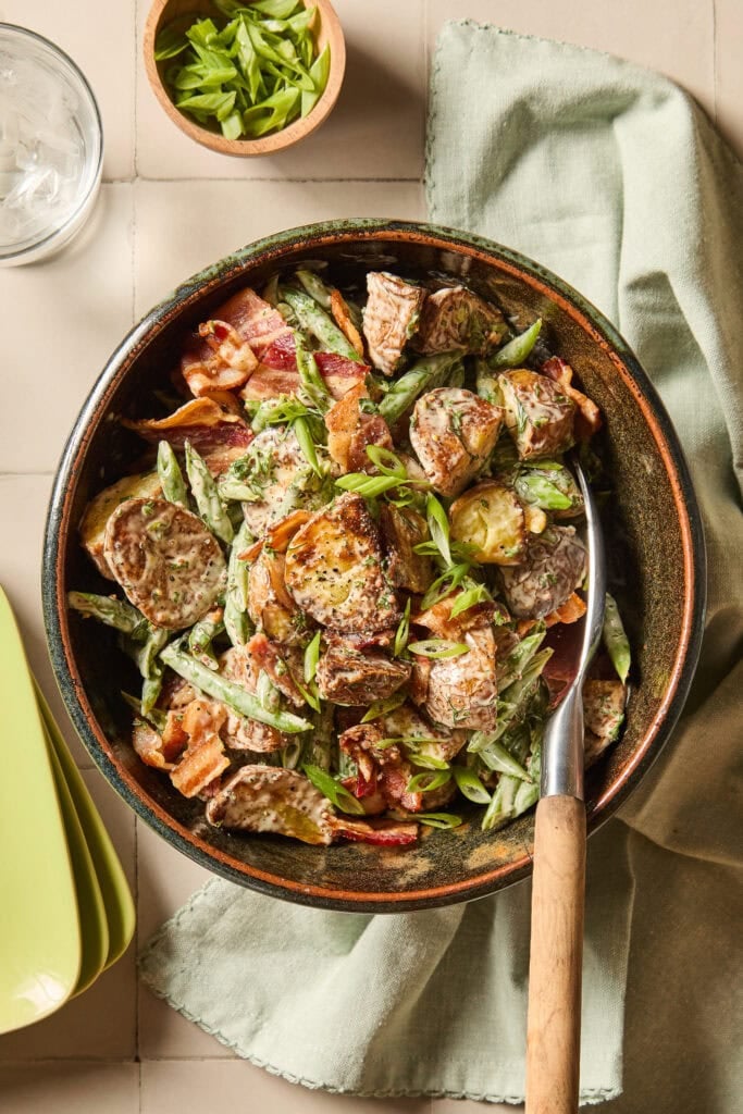 A bowl full of green bean and potato salad in a bowl on a tiled table.