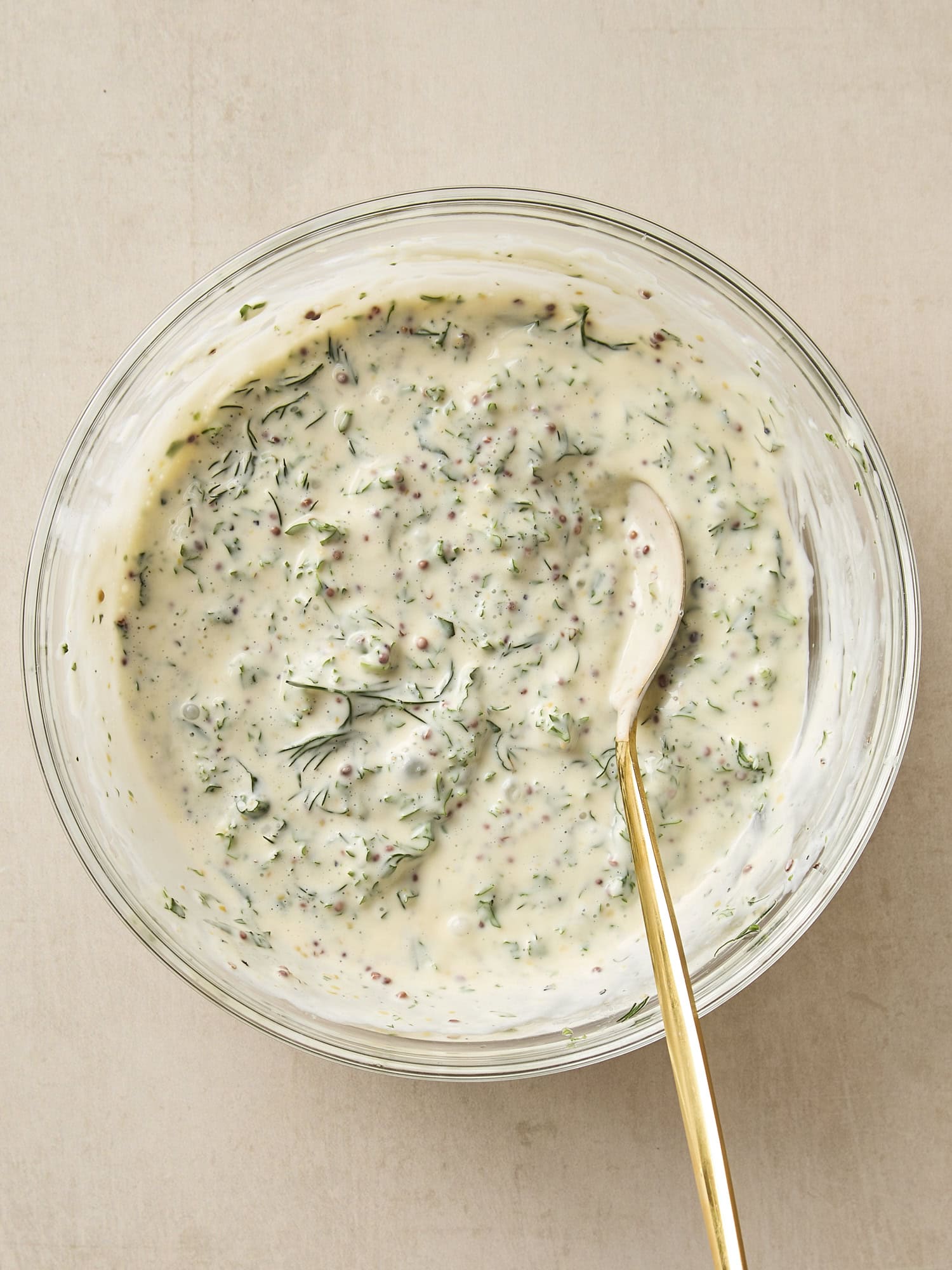 Mustard, herb, and mayo potato salad dressing in a glass bowl.