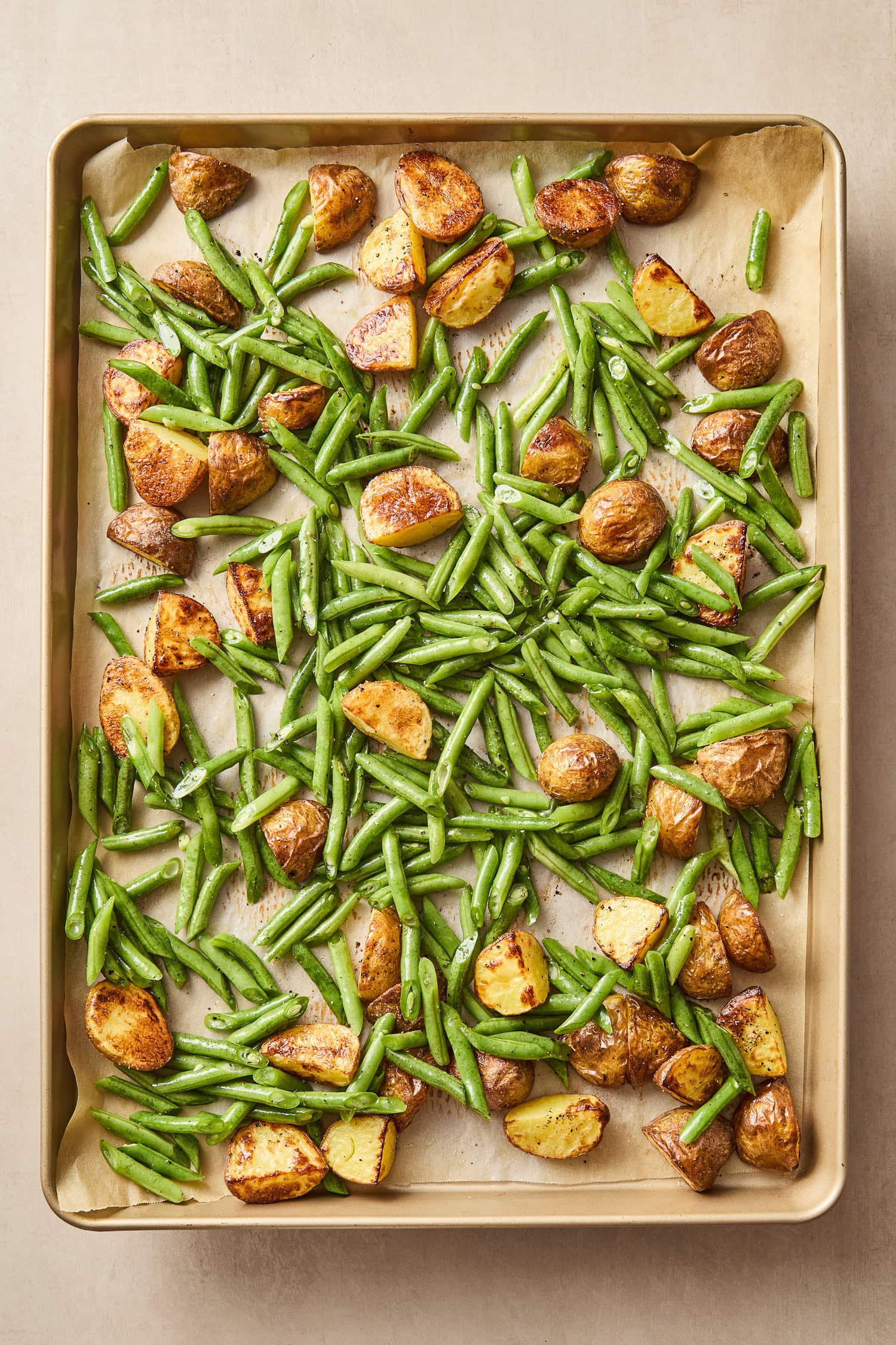 Green beans and potatoes rest on a baking sheet after roasting.