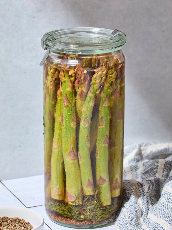 Glass jar filled with quick pickled asparagus on tile surface.