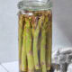 Glass jar filled with quick pickled asparagus on tile surface.