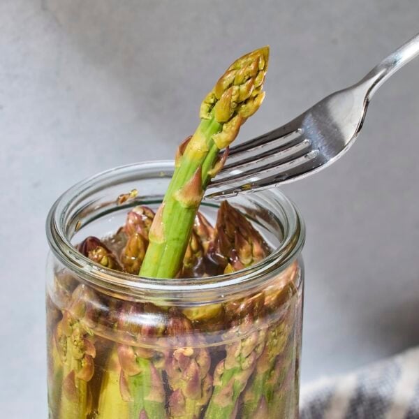Fork pulling up spear of pickled asparagus from jar.