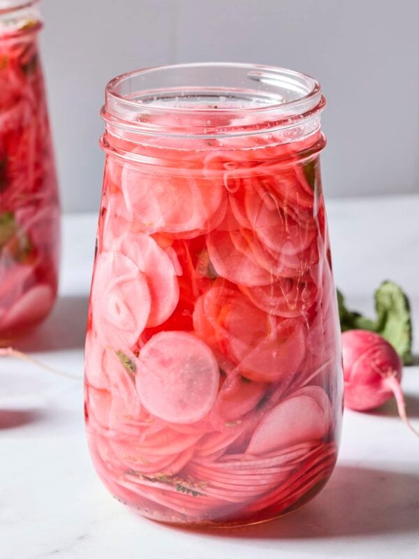 Glass jar filled with sliced pickled radishes with cilantro and scallion in jar.