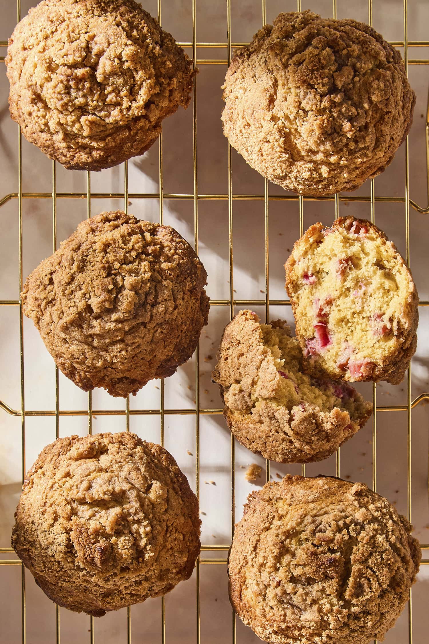 Wire cooling rack with rhubarb muffins after baking with one broken in half.