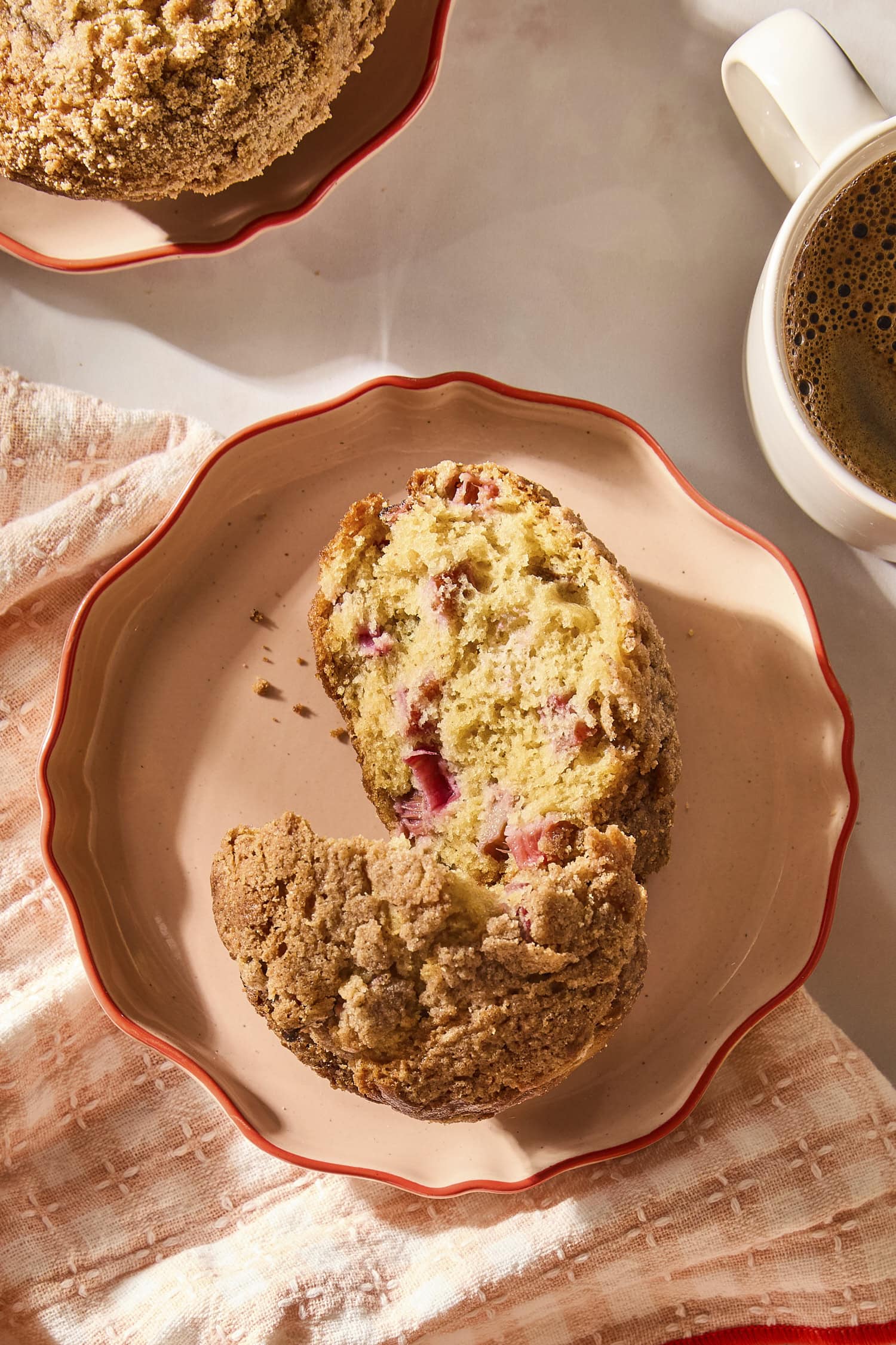 Plate with rhubarb muffin sliced in half with morning sunlight and cup of coffee.