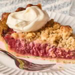 White plate with fork and slice of strawberry rhubarb pie with dollop of whipped cream.