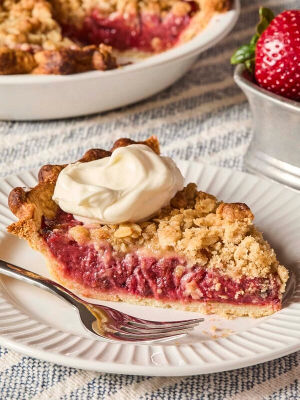 Slice of roasted strawberry rhubarb pie on plate with dollop of whipped cream on top.
