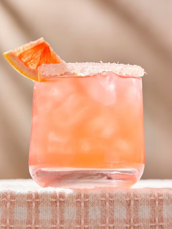 Light pink grapefruit-forward siesta cocktail sitting on surface with grapefruit slice.