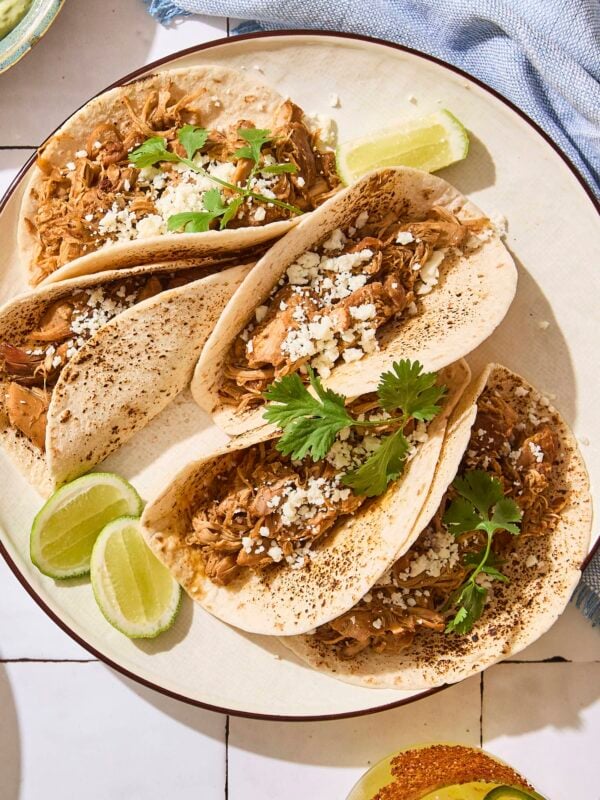 Four chicken tacos on a plate in bright sunlight.
