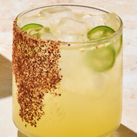 Glass with tajin on rim filled with spicy margarita with jalapenos in glass.